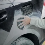 затирает шпатлевку на крыле автомобиля